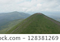 Aerial view of the approaching mountain peak against the backdrop of a beautiful mountain landscape and cloudy blue sky. Many travelers can be seen at the top of the mountain. 128381269
