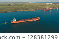 Aerial view of a large cargo ship leaving the harbor with tugboats at sunset. On the horizon in the roadstead there are ships waiting for the entrance to the port. 128381299