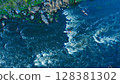 Aerial view of a kayak boat rushing along with a stormy stream between the stones at high speed. Rowers trying to steer the boat in the right direction. 128381302