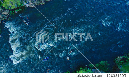 Aerial view of a kayak boat rushing along a turbulent river between stone rocks at high speed. Athletes trying to steer the boat in the right direction. Aerial view of a kayak boat rushing along a turbulent river between stone rocks at high speed. Athletes trying to steer the boat in the right direction. 128381305