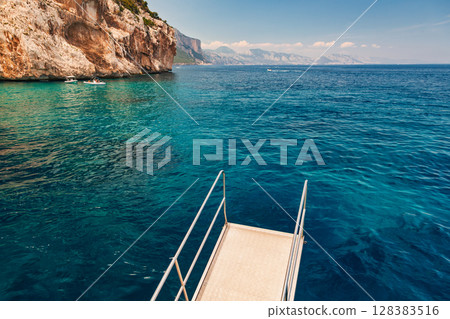 Diving platform overlooking turquoise sea and rugged cliffs of Gulf of Orosei on Sardinian east coast Diving platform overlooking turquoise sea and rugged cliffs of Gulf of Orosei on Sardinian east coast 128383516