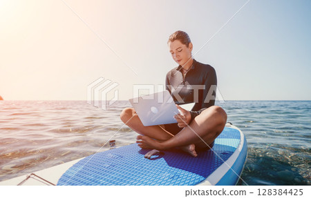 Woman Laptop Paddleboard Ocean - Woman working on laptop while paddleboarding on the ocean. 128384425