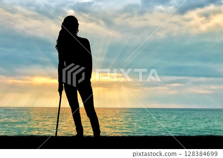 A silhouette of a woman supports herself with a crutch A silhouette of a woman supports herself with a crutch 128384699