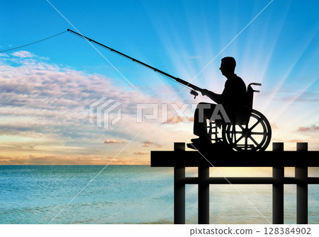 Silhouette of a disabled man in a wheelchair with a fishing rod in his hand fishing near the water on the pier 128384902
