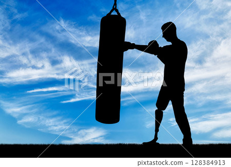 Silhouette of a disabled man with a leg prosthesis, training with a punching bag 128384913
