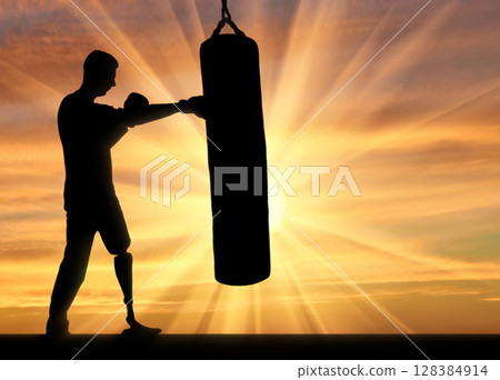 Silhouette of a disabled man with a leg prosthesis, training with a punching bag Silhouette of a disabled man with a leg prosthesis, training with a punching bag 128384914