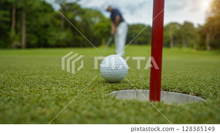 Golfer putting ball on the green golf, lens flare on sun set evening time. Golfer hitting golf ball. 128385149