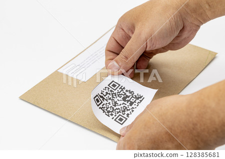 Person is attaching QR code label to brown envelope, demonstrating modern and efficient way to manage information. hands are carefully placing label, indicating attention to detail Person is attaching QR code label to brown envelope, demonstrating modern and efficient way to manage information. hands are carefully placing label, indicating attention to detail 128385681