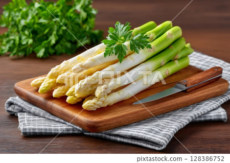 Fresh white and green asparagus lying on wooden cutting board 128386752