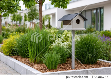 Birdhouse standing in a flowerbed in the garden of a modern residential building 128386783