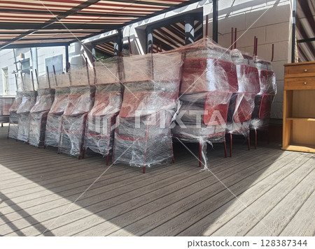 Stacked chairs wrapped in plastic film suggesting closed cafe or restaurant 128387344