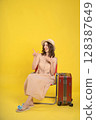 Traveler Sitting on a Chair with Luggage Against a Yellow Background 128387649