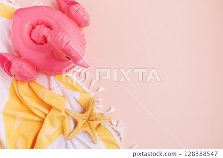Beach essentials including an inflatable flamingo, starfish, and towel on a light background. 128388547