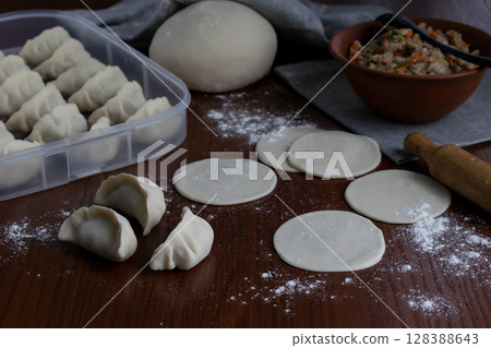 Homemade pork gyoza dumplings preparation with raw dough circles and filling on wooden surface flour and rolling pin visible traditional Japanese food cooking process close up kitchen scene 128388643
