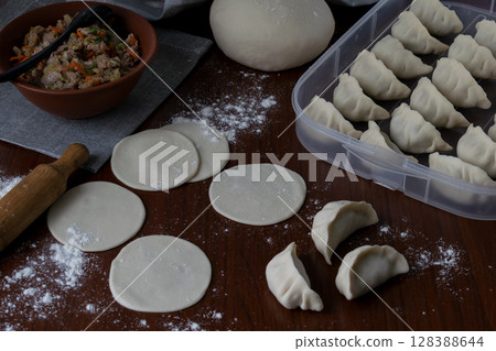 Raw dough rounds on wooden table with flour and rolling pin before filling for homemade pork gyoza preparation process traditional Japanese dumplings making step kitchen view food concept Raw dough rounds on wooden table with flour and rolling pin before filling for homemade pork gyoza preparation process traditional Japanese dumplings making step kitchen view food concept 128388644