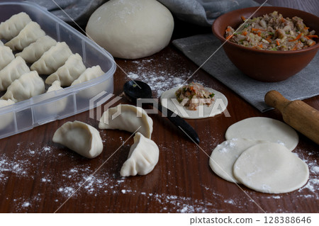 Making gyoza dumplings at home with pork and vegetable filling visible stages of shaping and folding on wooden table floured surface traditional Japanese cooking food preparation process Making gyoza dumplings at home with pork and vegetable filling visible stages of shaping and folding on wooden table floured surface traditional Japanese cooking food preparation process 128388646