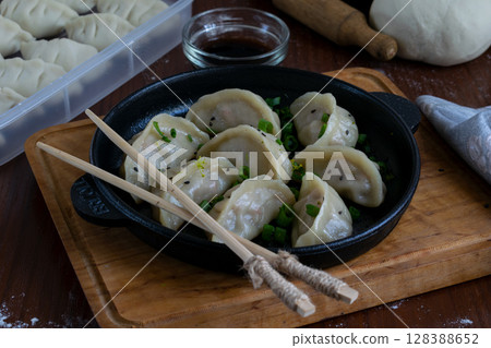 Pan fried Japanese pork gyoza served on black plate with dipping sauce on wooden tray garnished with green onion chopsticks traditional meal presentation ready to eat top view Pan fried Japanese pork gyoza served on black plate with dipping sauce on wooden tray garnished with green onion chopsticks traditional meal presentation ready to eat top view 128388652