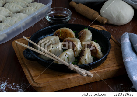Cooked gyoza dumplings with pork filling served on cast iron pan with dipping sauce wooden tray napkin traditional Japanese dish hot meal top view close up with chopsticks Cooked gyoza dumplings with pork filling served on cast iron pan with dipping sauce wooden tray napkin traditional Japanese dish hot meal top view close up with chopsticks 128388653