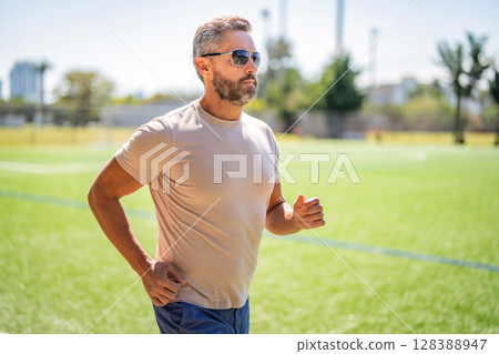 Sport runner in city park. The sportsman running in summer day. Man sportsman running for exercise in active wear. Sportsman jogger running and wearing sunglasses. Sport run Sport runner in city park. The sportsman running in summer day. Man sportsman running for exercise in active wear. Sportsman jogger running and wearing sunglasses. Sport run 128388947