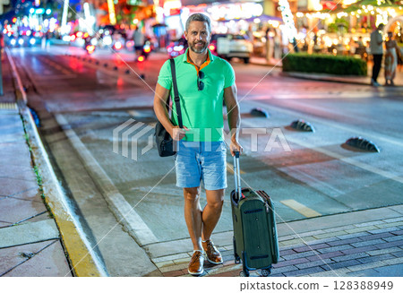 Man travel abroad weekend. Travel lifestyle. Tourist in summer city. Travel bag. Summer trip in America. Mature tourist in night Miami. Traveler man in casual clothes with suitcase. Night flight Man travel abroad weekend. Travel lifestyle. Tourist in summer city. Travel bag. Summer trip in America. Mature tourist in night Miami. Traveler man in casual clothes with suitcase. Night flight 128388949