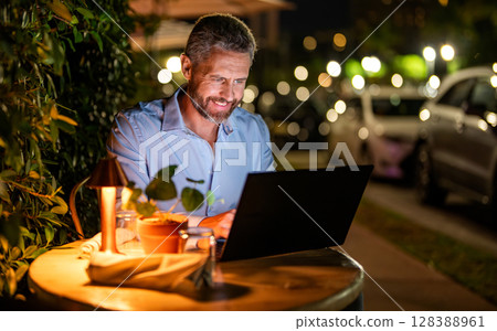 Successful businessman freelancing online. Business success. Businessman working on laptop outdoor. Business man having video laptop call in the evening cafe. Business man working online, copy space 128388961
