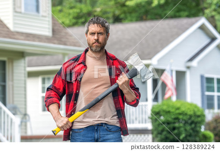 Lumberjack sweating hold heavy axe. Strong man work in neighborhood. Lumberjack men with axe. Lumberjack carries axe. Handsome man with axe. Lumberjack at suburban house with ax 128389224
