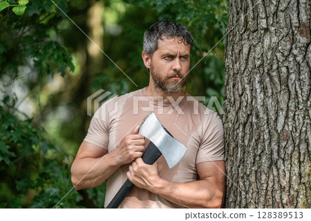 Lumberjack carries axe. Sweating after hard work. Handsome man with axe. Lumberjack in woods with ax. Lumberjack in shirt with heavy axe. Strong man work in forest. Lumberjack men in forest with axe 128389513
