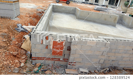 Beginning stages of a residential pool construction project are shown, focusing on the cement foundation being formed. Workers prepare the area for the next phases of construction. Beginning stages of a residential pool construction project are shown, focusing on the cement foundation being formed. Workers prepare the area for the next phases of construction. 128389524