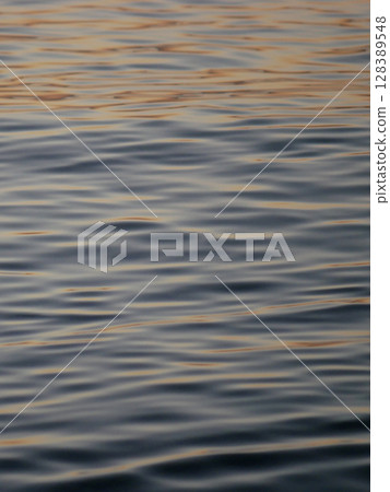 A tranquil close-up of gently rippling water illuminated by warm, golden light from a sunset. Wave pattern for wellness, nature, or background theme concepts A tranquil close-up of gently rippling water illuminated by warm, golden light from a sunset. Wave pattern for wellness, nature, or background theme concepts 128389548