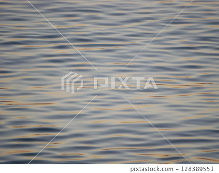 A tranquil close-up of gently rippling water illuminated by warm, golden light from a sunset. Wave pattern for wellness, nature, or background theme concepts 128389551