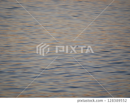 A tranquil close-up of gently rippling water illuminated by warm, golden light from a sunset. Wave pattern for wellness, nature, or background theme concepts 128389552