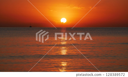 Vivid sunset over the sea with a glowing sun and golden reflection on the calm water. Peaceful and captivating atmosphere. Nature background, relaxation concept, travel theme and inspirational visual 128389572