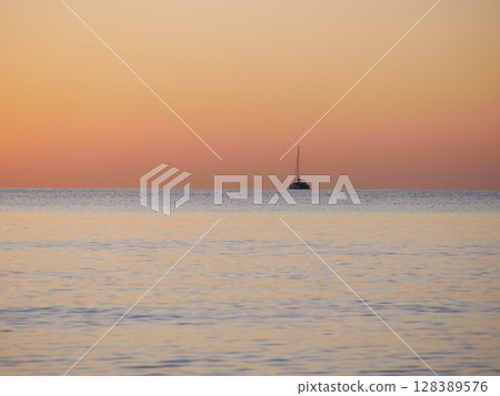 A breathtaking sunset over the calm sea with a sailboat on the horizon. Warm orange and golden tones fill the sky and reflect on the water. Travel, nature, relaxation, and maritime concept A breathtaking sunset over the calm sea with a sailboat on the horizon. Warm orange and golden tones fill the sky and reflect on the water. Travel, nature, relaxation, and maritime concept 128389576