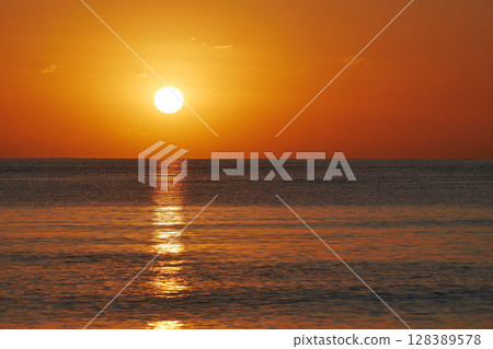 Vivid sunset over the sea with a glowing sun and golden reflection on the calm water. Peaceful and captivating atmosphere. Nature background, relaxation concept, travel theme and inspirational visual 128389578