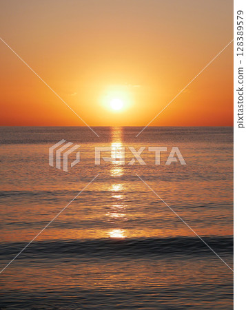Vivid sunset over the sea with a glowing sun and golden reflection on the calm water. Peaceful and captivating atmosphere. Nature background, relaxation concept, travel theme and inspirational visual 128389579