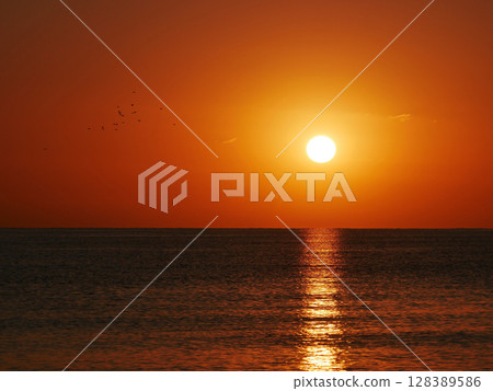 Vivid sunset over the sea with a glowing sun and golden reflection on the calm water. Peaceful and captivating atmosphere. Nature background, relaxation concept, travel theme and inspirational visual 128389586