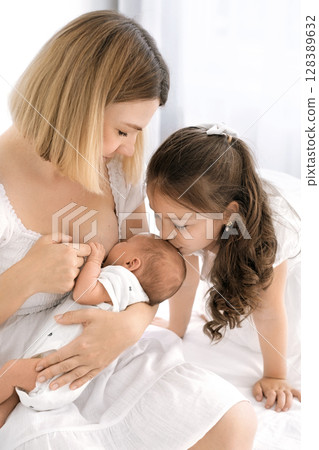 A mother breastfeeds a newborn baby. A little sister kisses her brother on the forehead while he eats. The benefits of breastfeeding A mother breastfeeds a newborn baby. A little sister kisses her brother on the forehead while he eats. The benefits of breastfeeding 128389632
