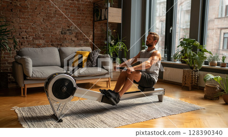 Determined man exercising using rowing machine in his modern apartment, promoting healthy lifestyle and home fitness 128390340