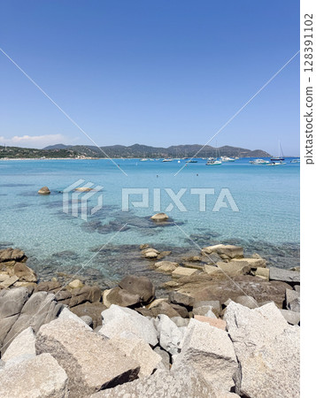 Serene coastal scene featuring clear blue waters, visible rocks, and distant boats under a clear sky. The tranquil setting invites relaxation and appreciation of natural beauty. Italy Sardinian 128391102