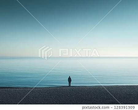 A lone individual stands on the shore, gazing at the tranquil sea. Soft morning light illuminates the serene landscape, creating a sense of stillness and reflection. 128391309