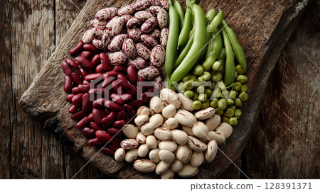 Colorful legumes spread across weathered wooden surface, displaying variety of kidney, cranberry, green beans and peas 128391371