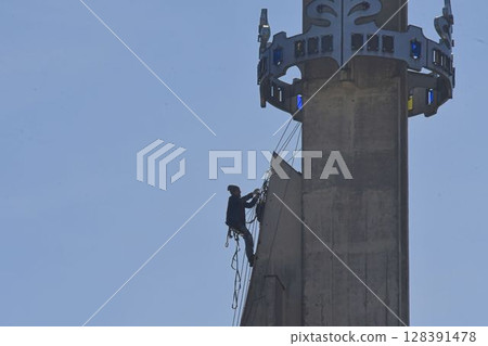 A skilled worker fixes the tower of a modern church. A roofer works on the tower of a modern building. The concept of working at height and safety at work A skilled worker fixes the tower of a modern church. A roofer works on the tower of a modern building. The concept of working at height and safety at work 128391478