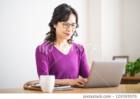 A middle-aged woman in her 50s working remotely in the living room at home 128393070