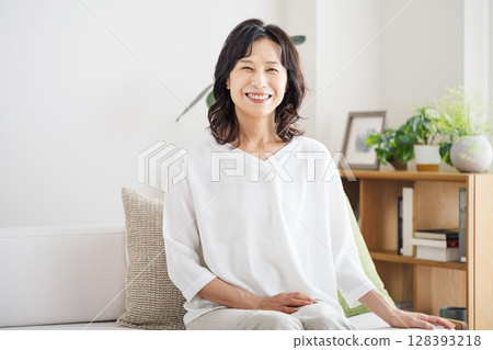 Portrait of a middle-aged woman in her 50s sitting on a sofa in the living room at home 128393218