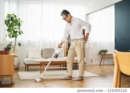 一名 50 多歲的中年男子正在家中吸塵 128393220