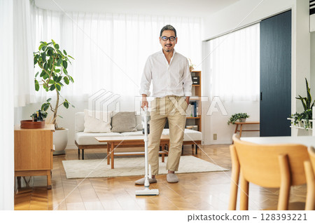 一名 50 多歲的中年男子正在家中吸塵 128393221