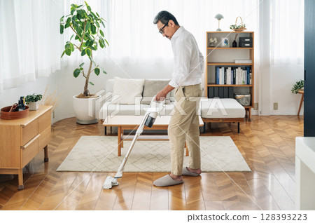 一位 50 多歲的中年男子正在打掃家裡的客廳 128393223