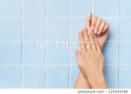 Beautiful womans hands with nude nail design on blue background. Manicure, pedicure beauty salon concept 128393296