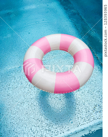 Swimming ring with pink and white stripes in a blue outdoor pool. Poolside atmosphere. Pink float. 128393965