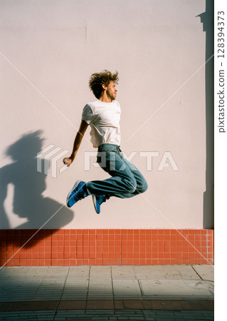 A man in a white shirt and blue jeans jumps in the air 128394373